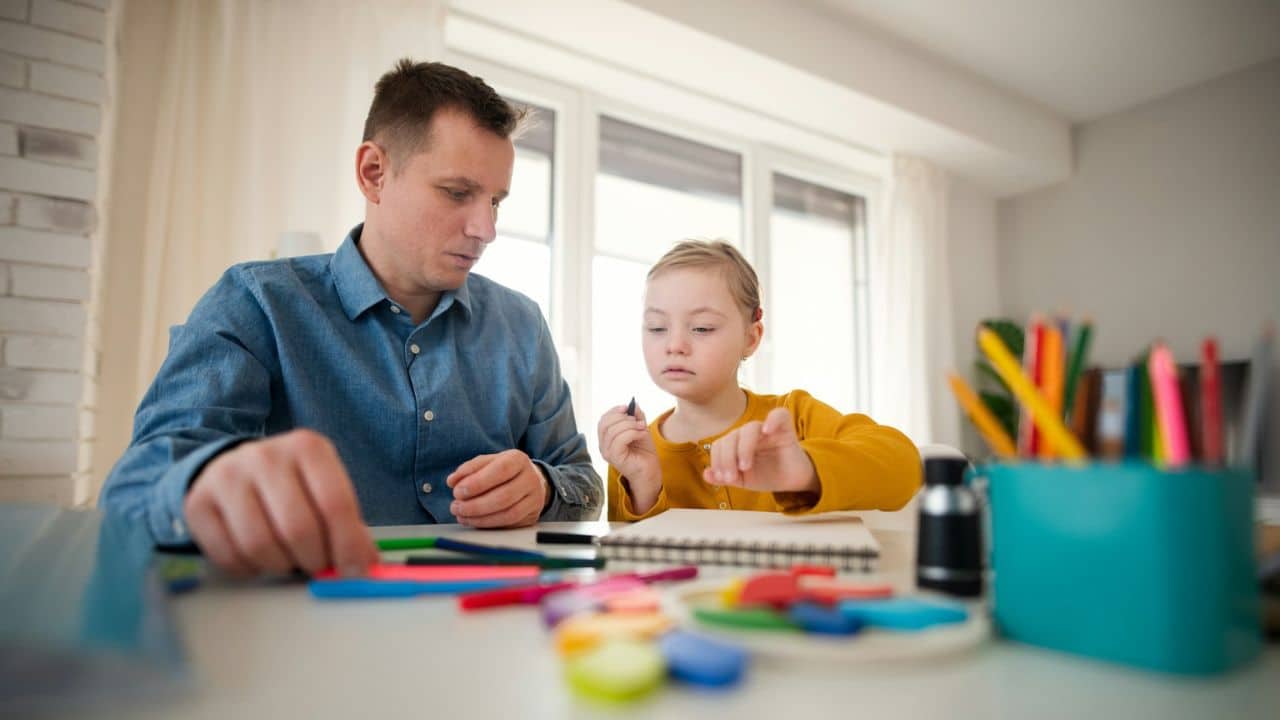 A man and a young girl are sitting at a table and drawing together.
