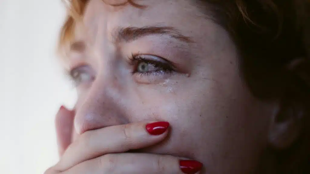 A crying woman with red nail polish, with her hand covering her mouth..