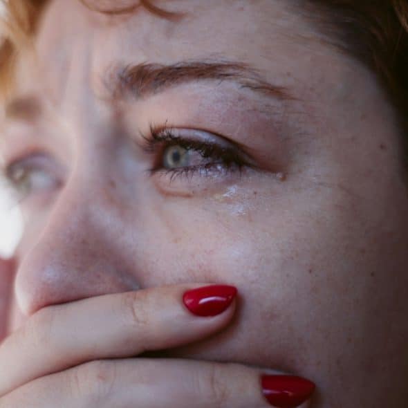 A crying woman with red nail polish, with her hand covering her mouth..