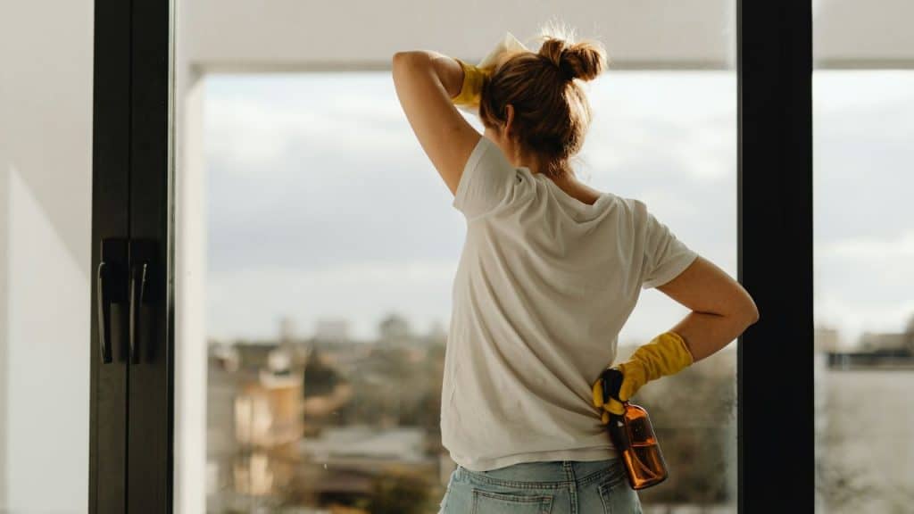 A woman with yellow gloves cleans a window with a spray bottle.