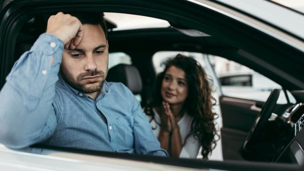 A woman with clasped hands looks apologetically at a man in a car.