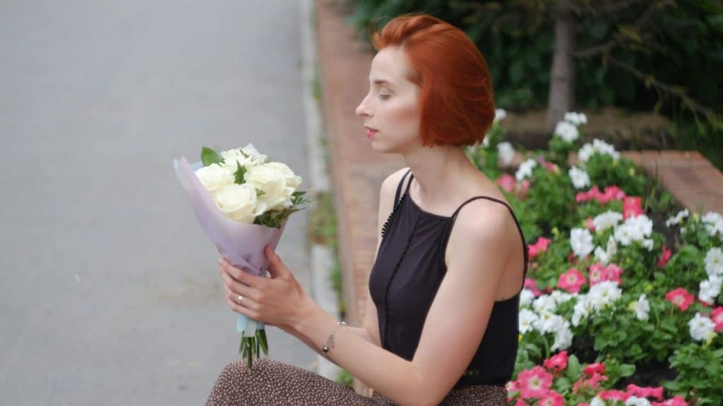 A woman with red hair looks at a bouquet of white roses.