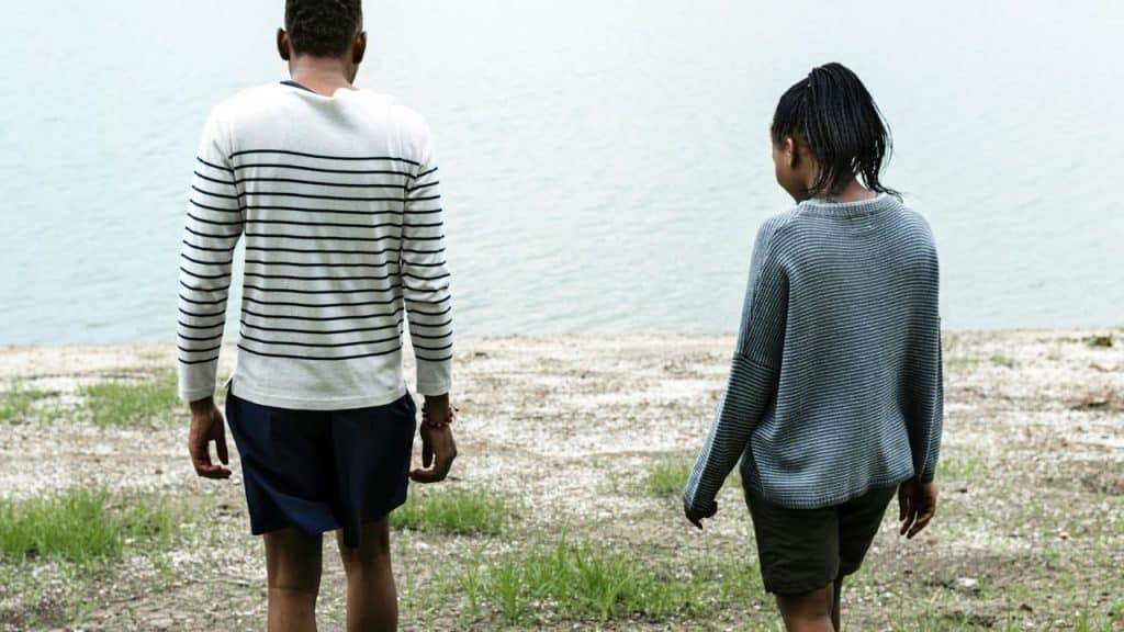 A couple stands apart from each other, looking at a body of water.
