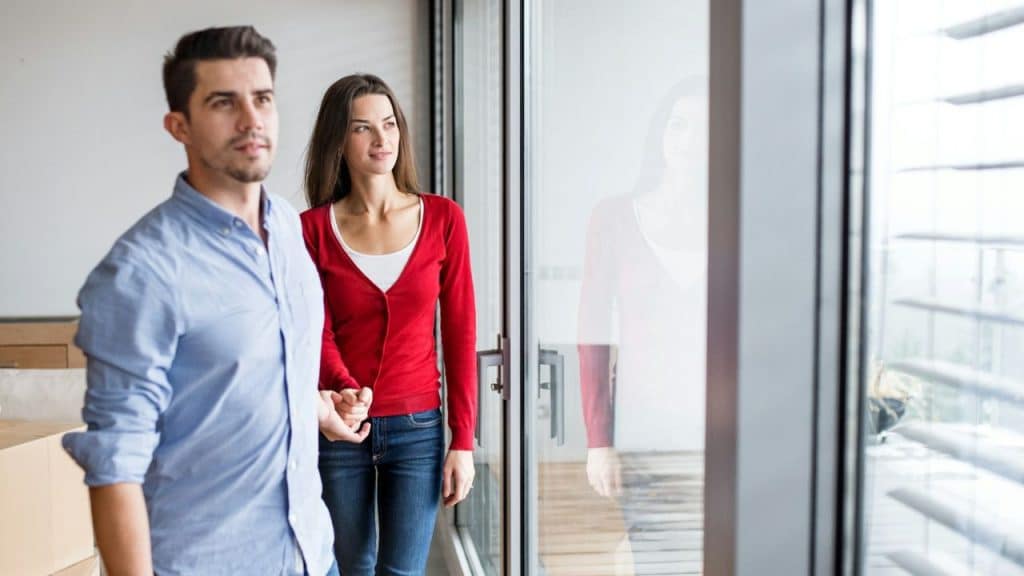 A man and woman hold hands and look out a large window together.
