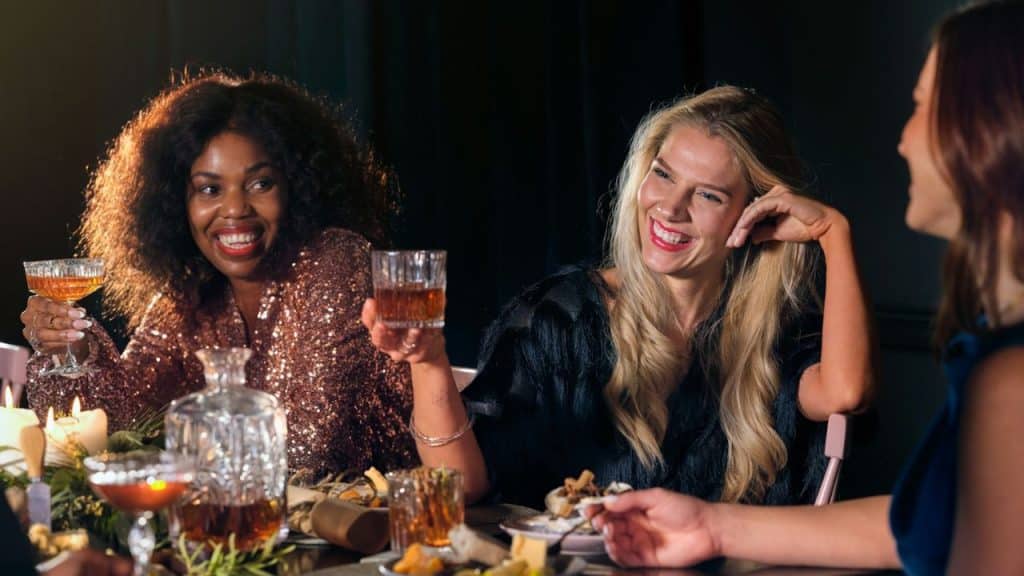 A group of smiling women at a dinner party holding drinks and talking to each other.