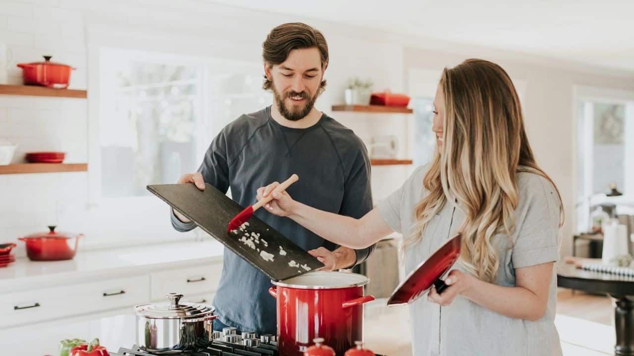 A man and a woman in a kitchen are smiling while cooking together.