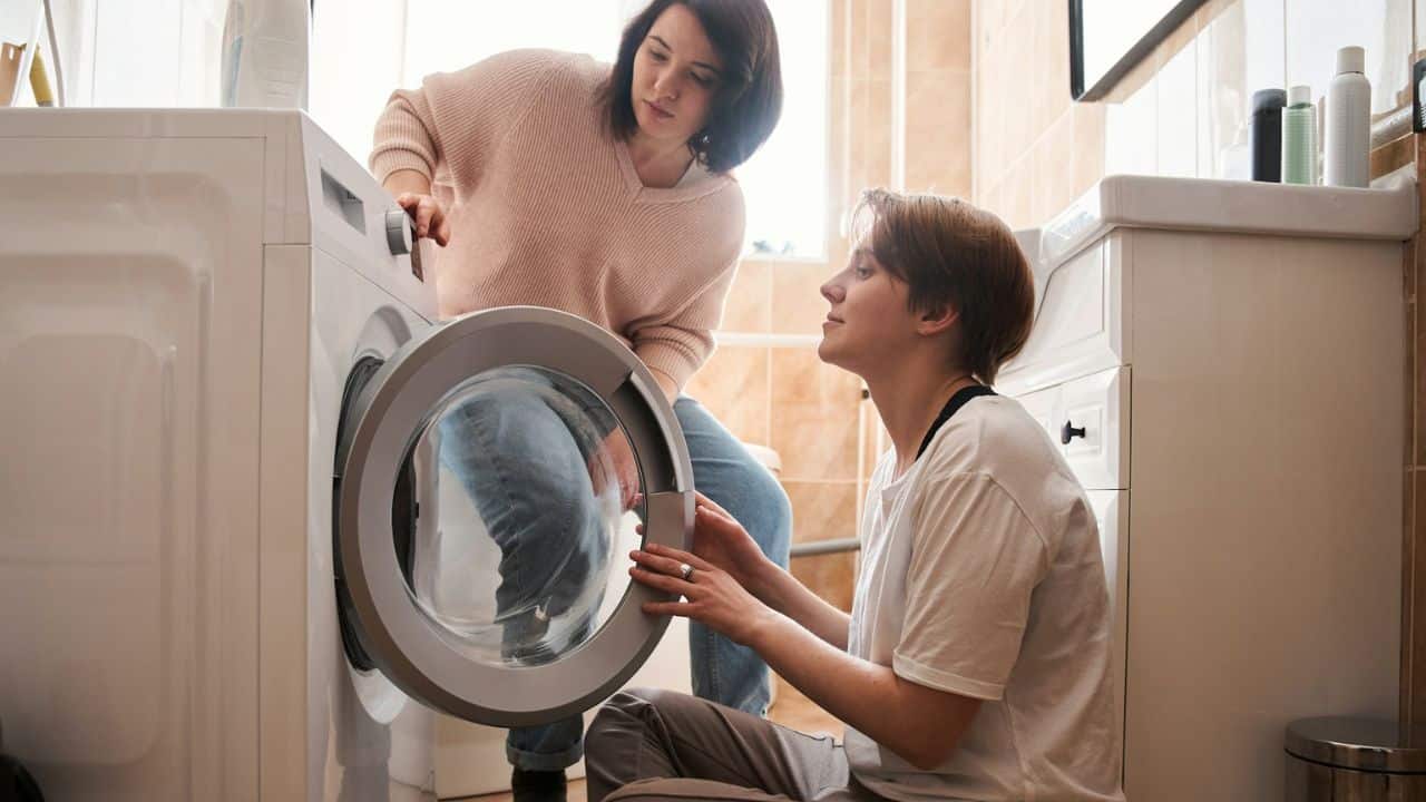 Two women are doing laundry, with one sitting on the floor and the other standing.