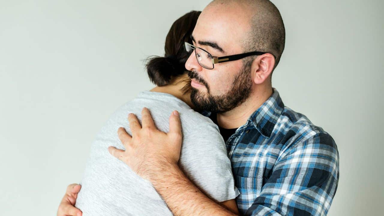 A man with glasses and a beard is hugging a person.