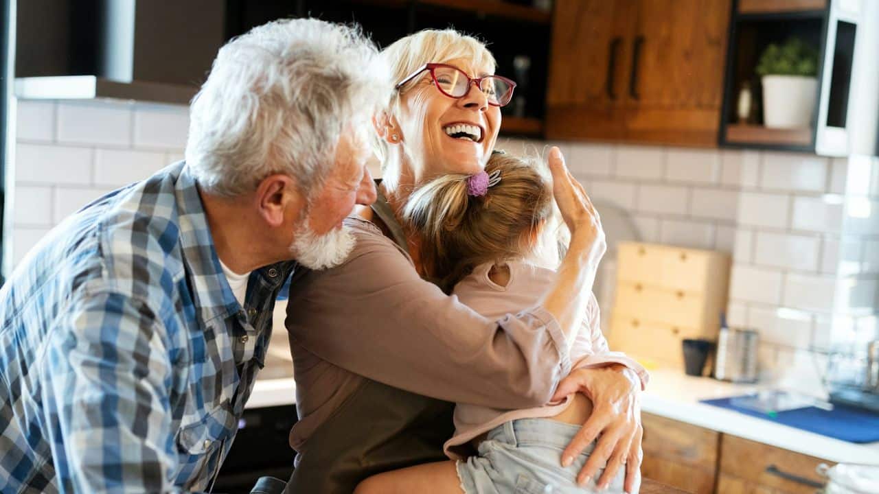 A laughing grandmother hugging a young girl, with a grandfather smiling at them.