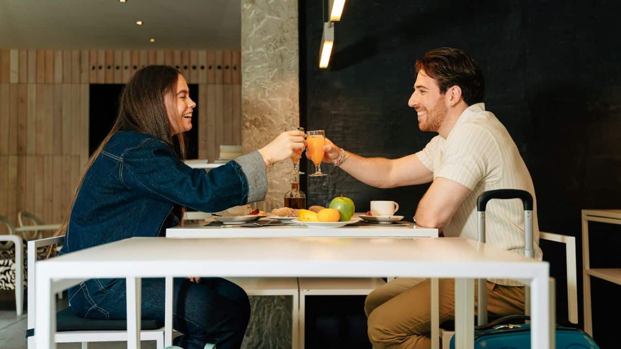 A happy couple toasting with juice at a table filled with food.