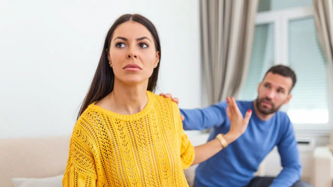 A woman looking away from a man who is trying to touch her arm.