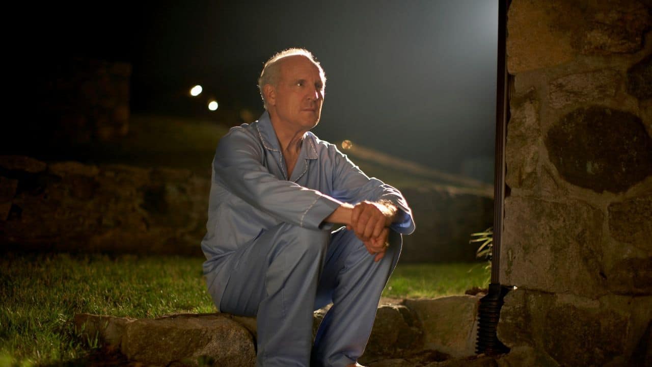 A senior man in blue pajamas sitting on rocks at night.