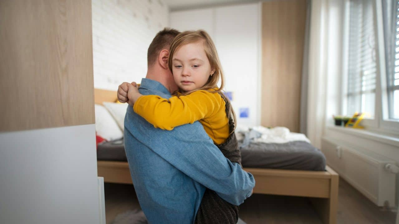 A concerned-looking father holding his daughter in his arms.