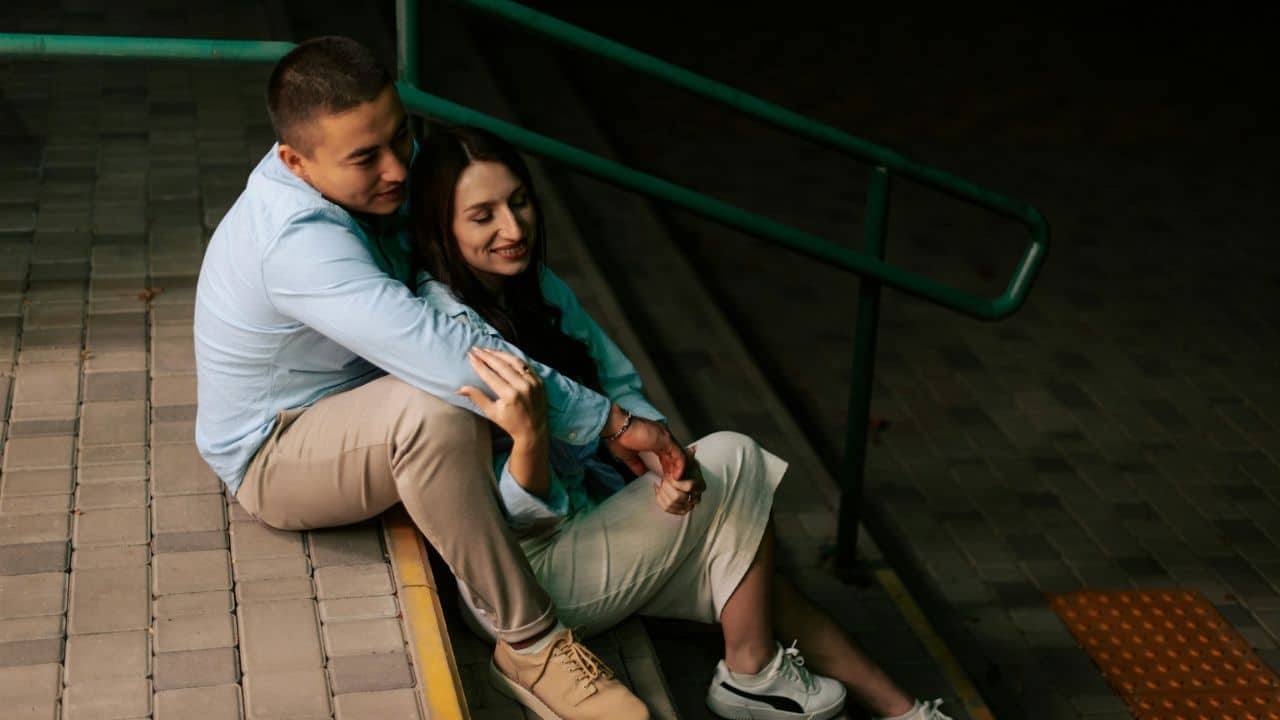 A happy couple is sitting on stairs, hugging each other and smiling.