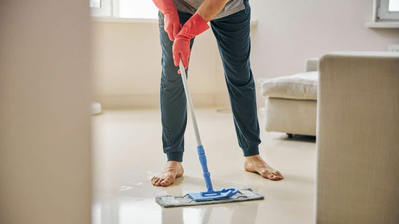 A barefoot person wearing pink gloves is mopping a floor.