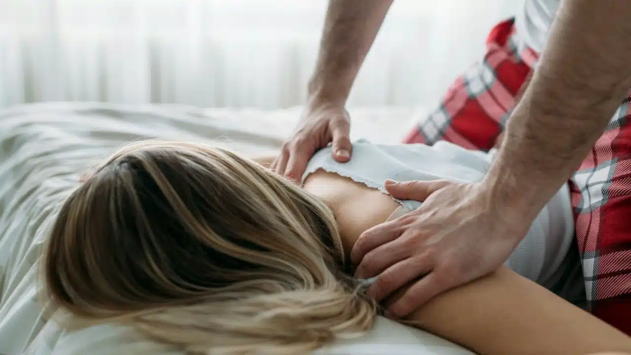 A person with a red-and-white plaid blanket is giving a shoulder massage to another person.