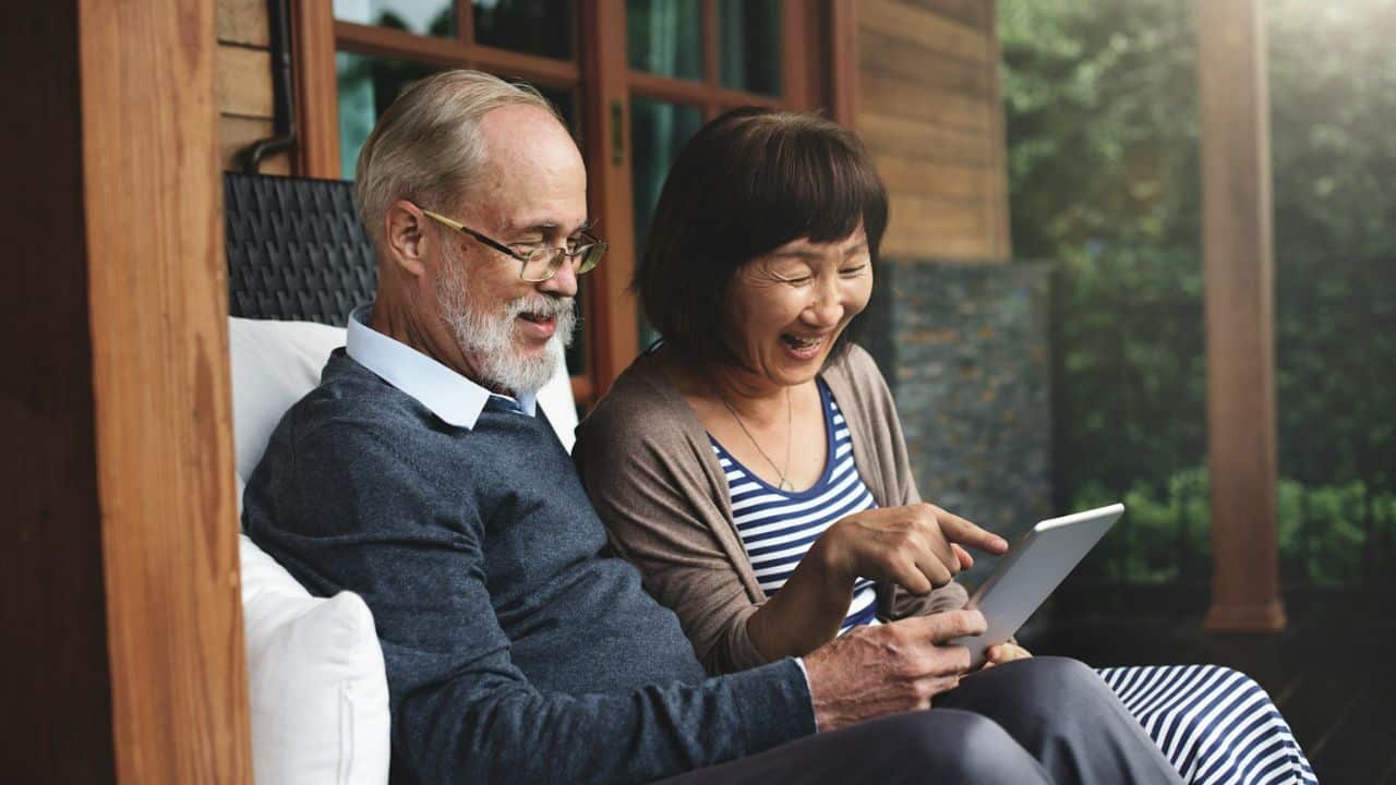 A laughing elderly couple looking at a tablet together.