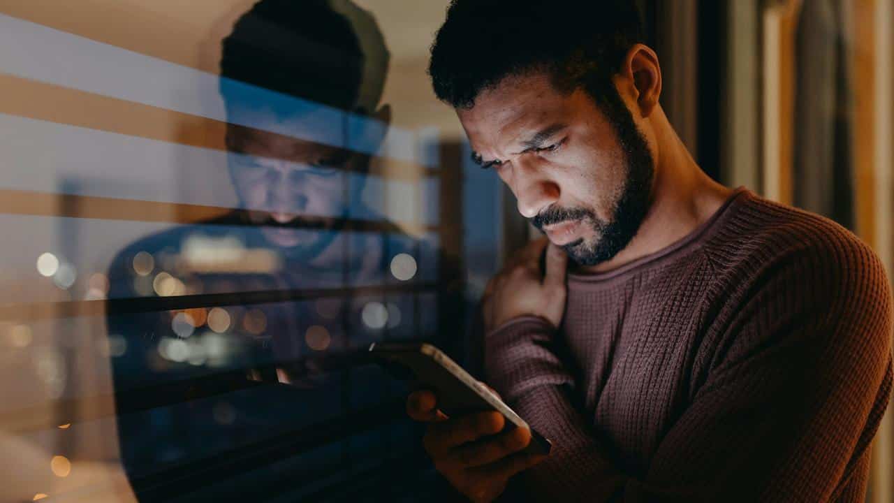 A man looking at his smartphone by a window at night.