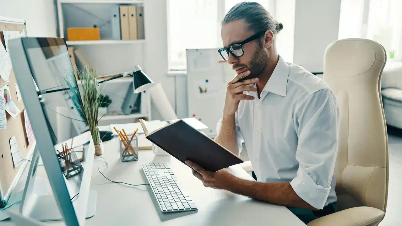 A man in an office reading a notebook at his desk.