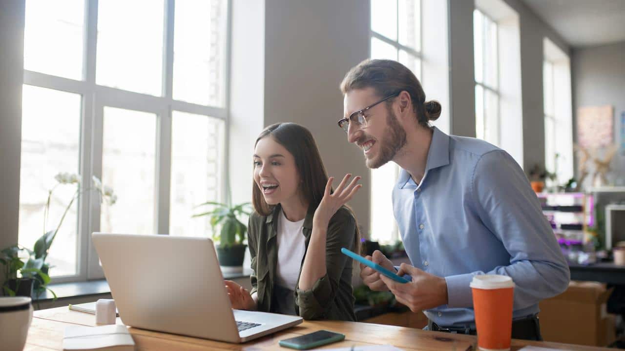 A man and woman smiling while looking at a laptop.