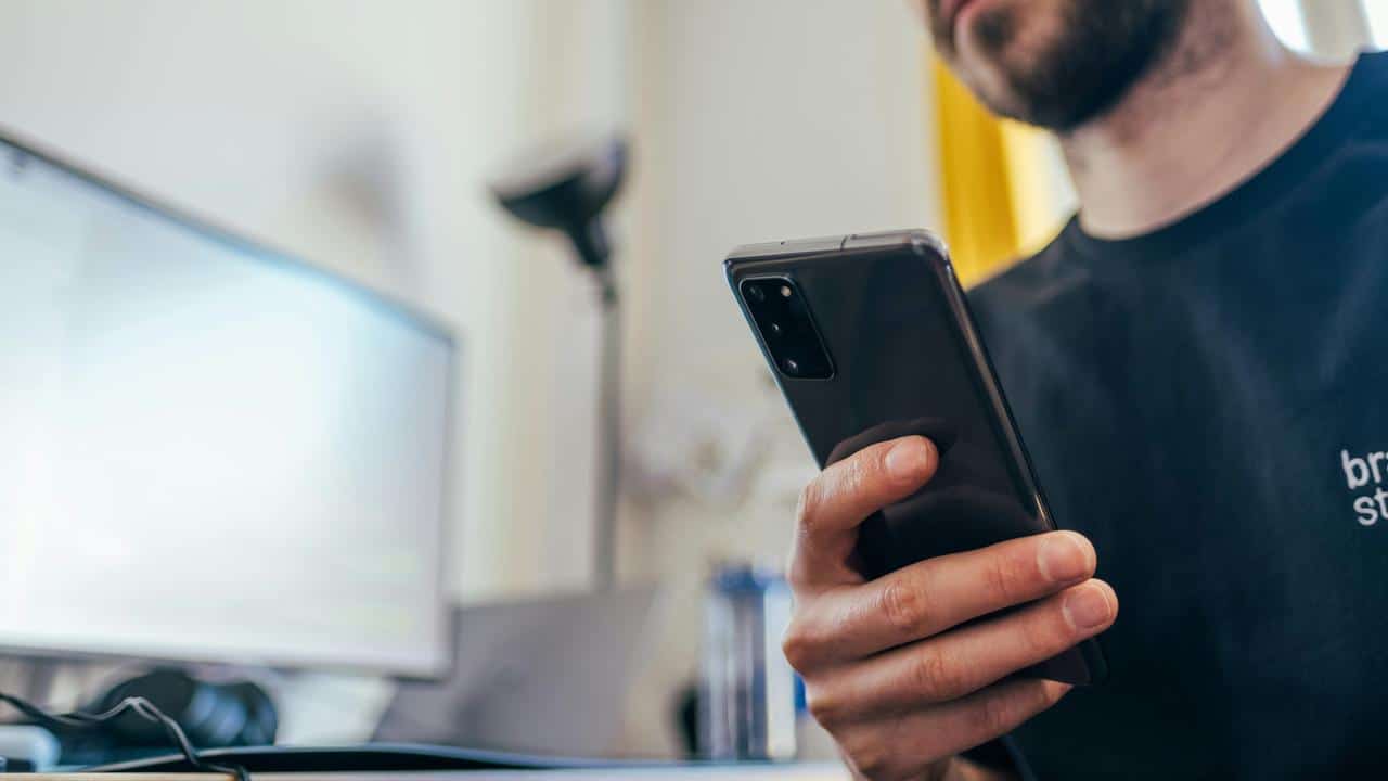 A man holding a smartphone at his desk.
