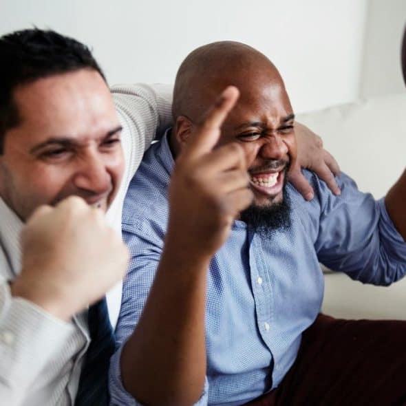A group of friends cheering while watching football indoors.