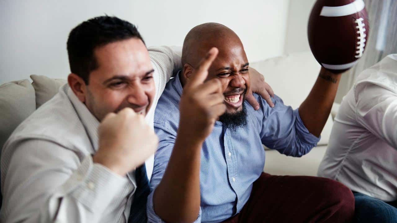 A group of friends cheering while watching football indoors.