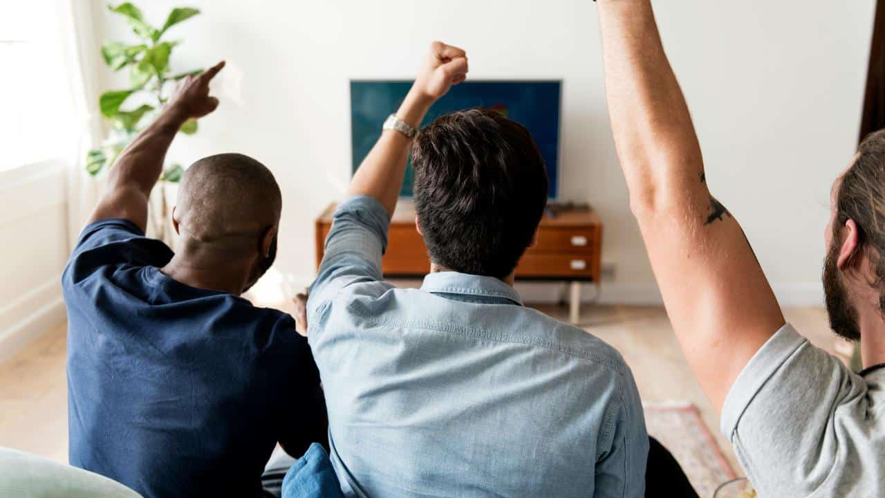 A group of men cheering at a TV.