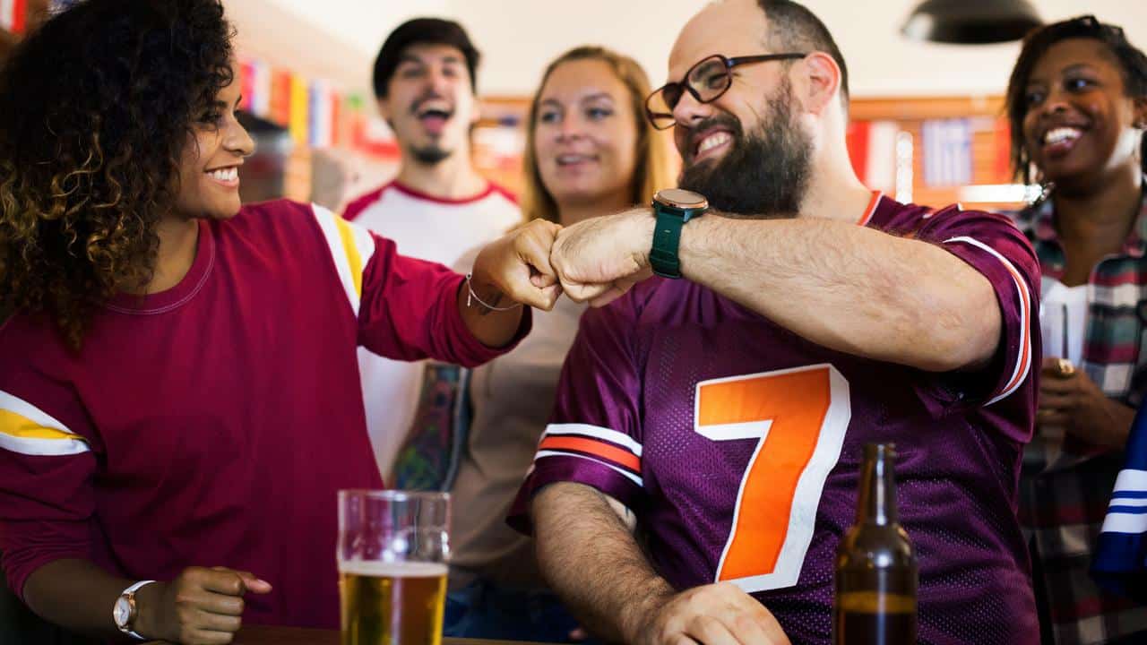 A group of friends fist bumping while watching a game.