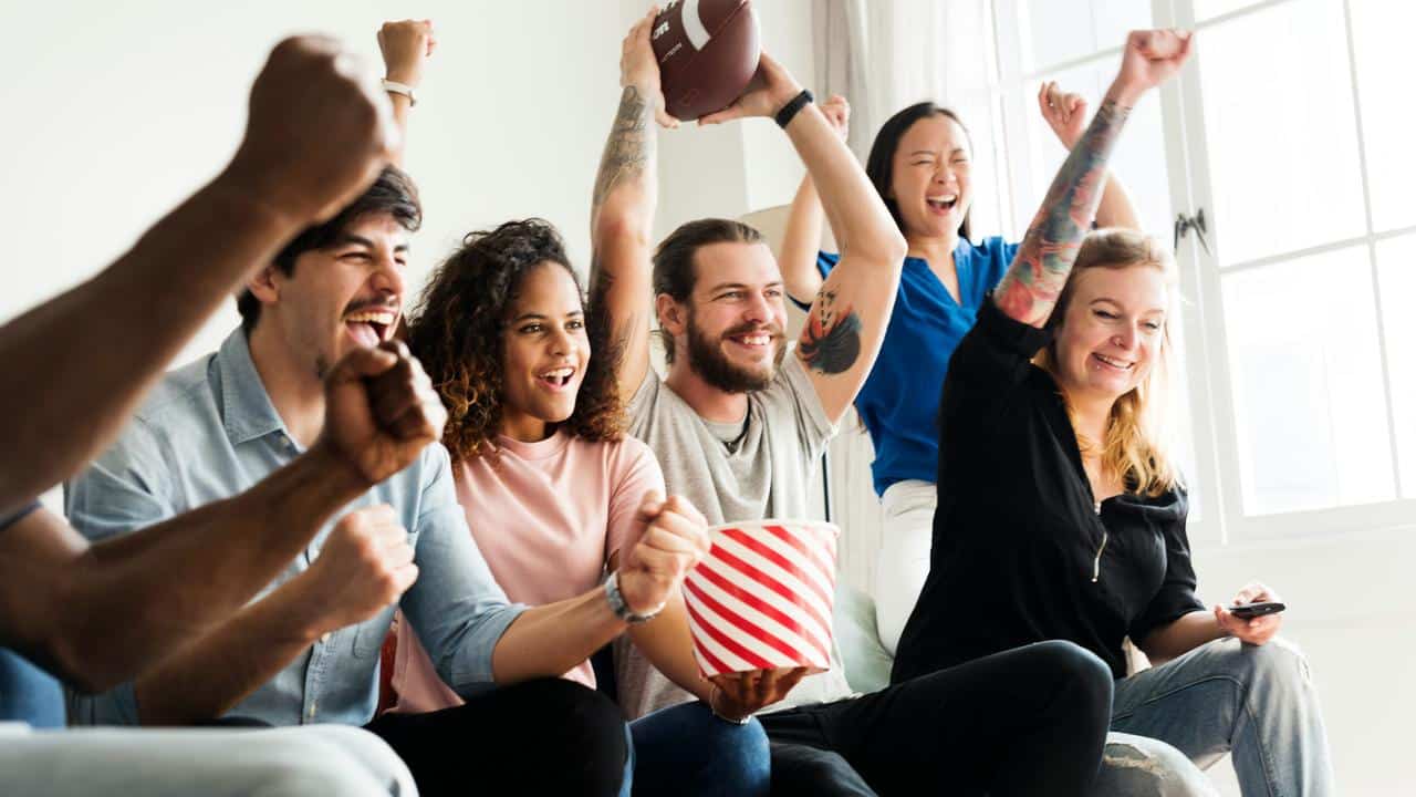 A group of friends cheering with a football and popcorn.