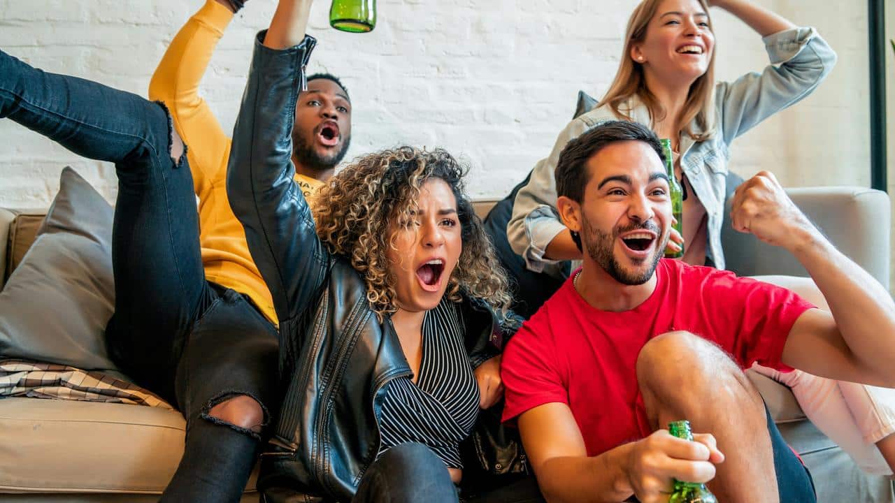 An excited group of friends cheering with drinks while watching a game.