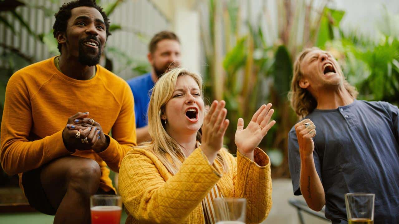 An enthusiastic group of friends cheering while watching a game outdoors.