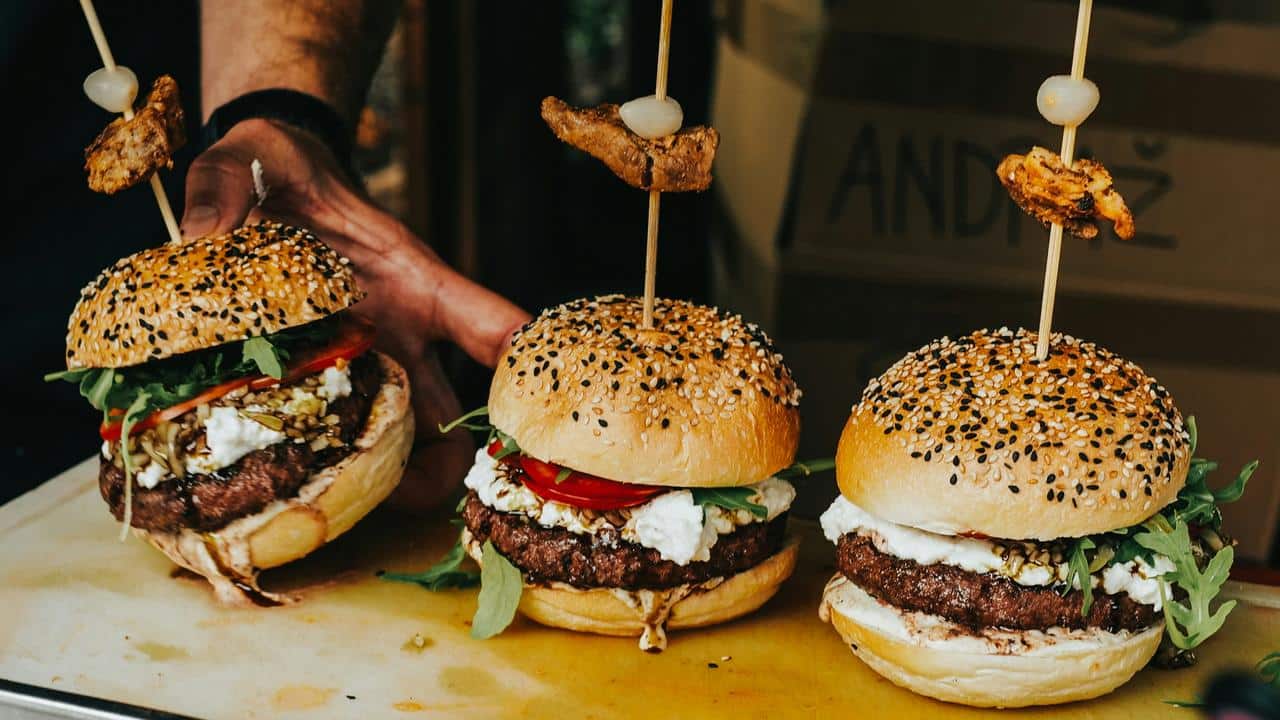 A row of gourmet burgers topped with skewers and sesame buns.