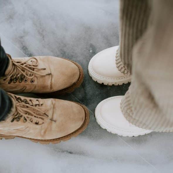 A close-up of two people standing on ice, wearing tan and white boots.