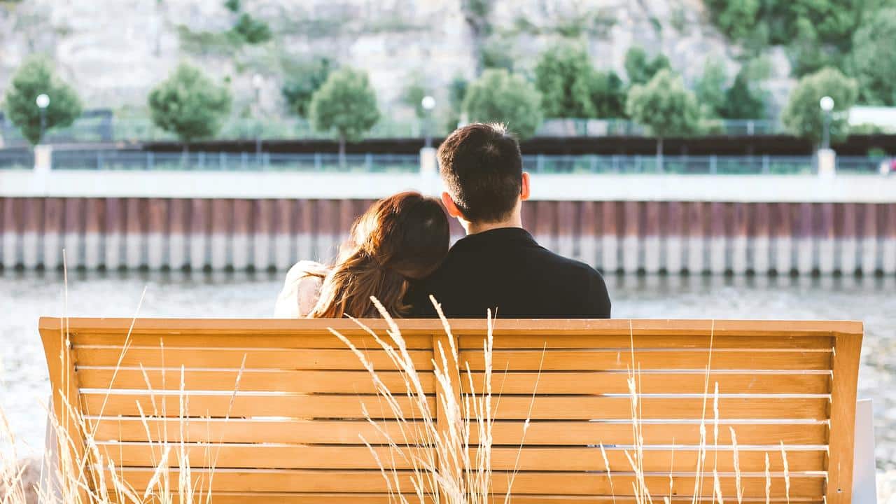 A couple sitting on a bench by the water.
