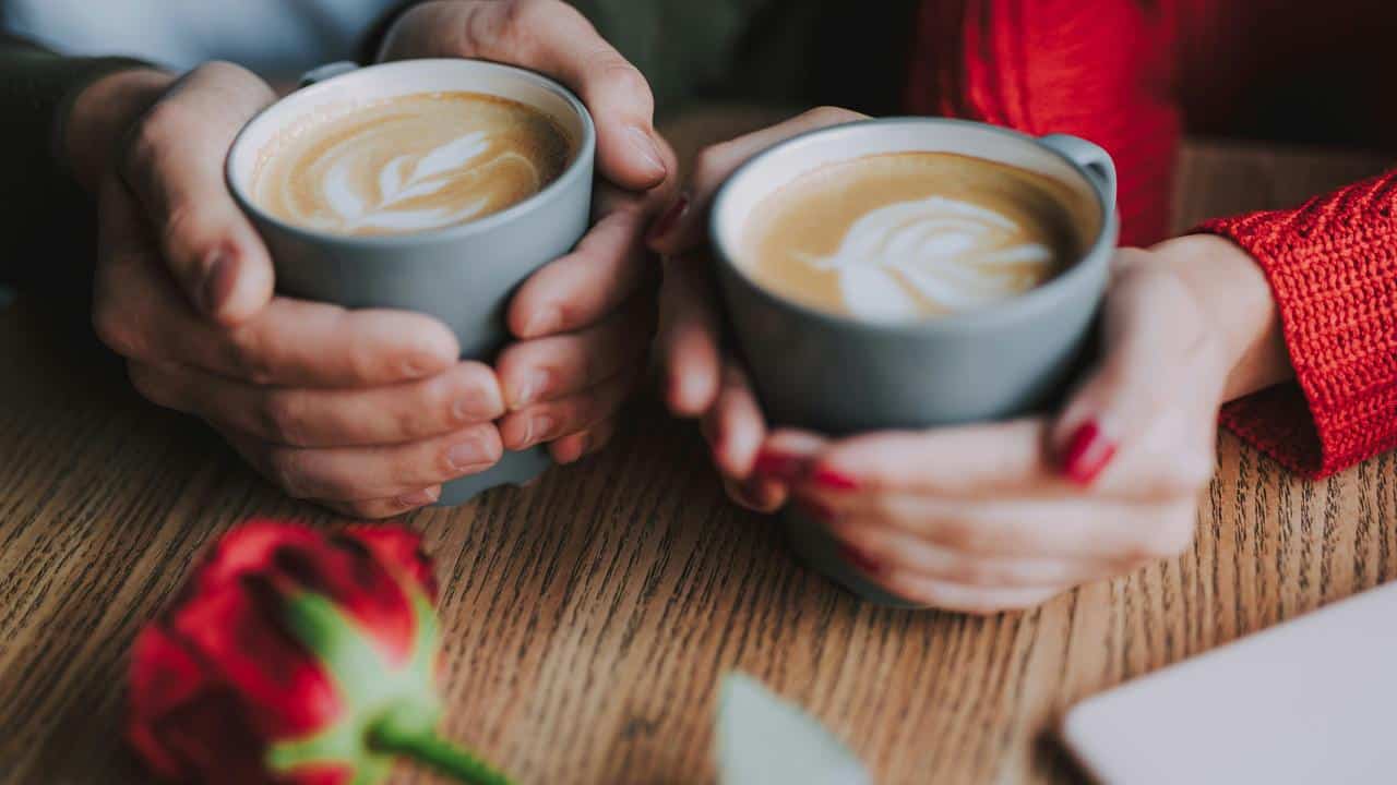 A couple holding coffee cups at a café table.