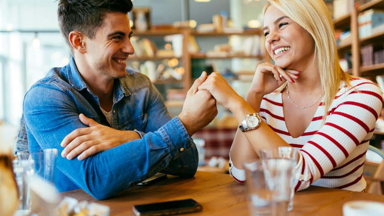 A couple laughing and holding hands at a café.