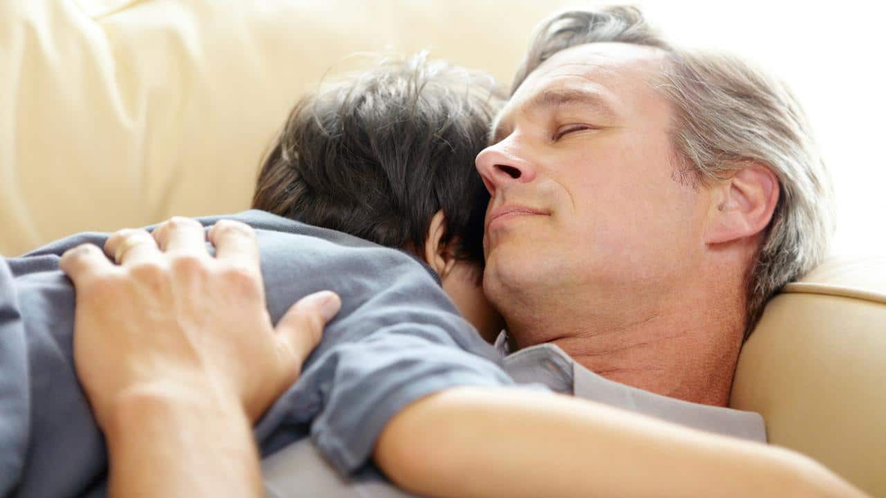 A man and child resting together on a couch.