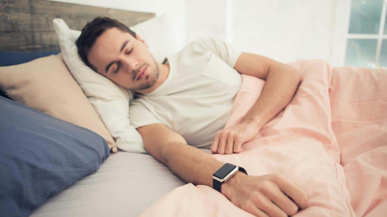 A man sleeping in bed while wearing a smartwatch.