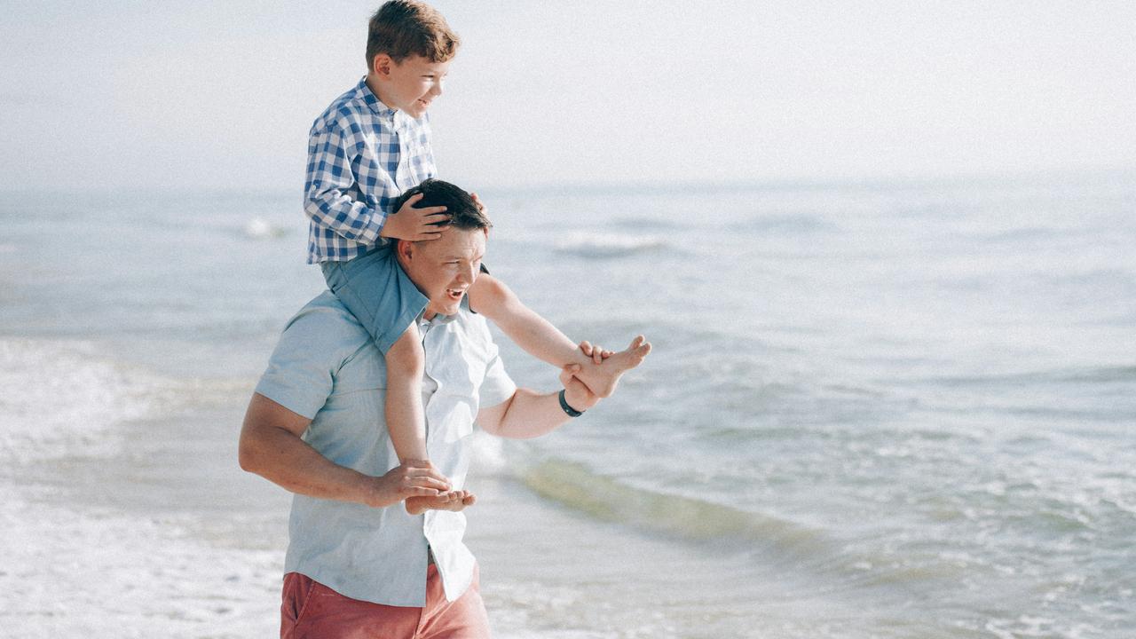 A man carrying a boy on his shoulders while walking on the beach.