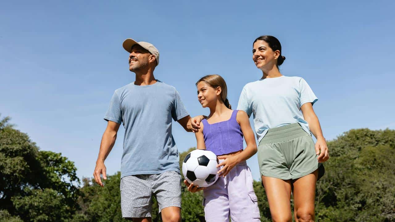 A family walking outdoors with a girl holding a soccer ball.