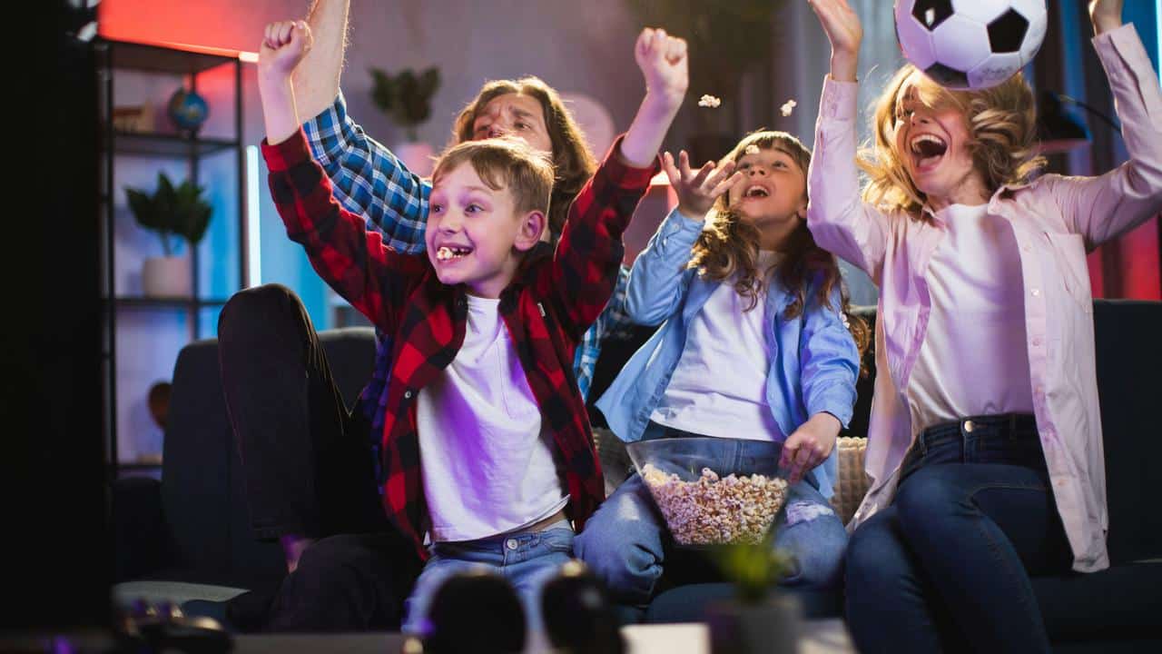 A family cheering while watching a soccer game on TV with popcorn.