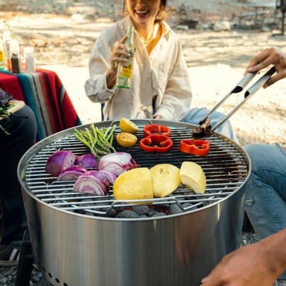 A group of friends grilling vegetables outdoors on a round barbecue grill.