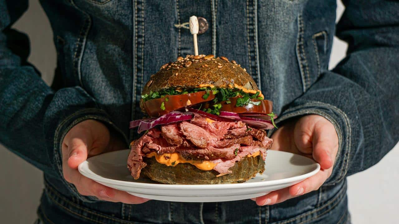 A person holding a large brisket sandwich.