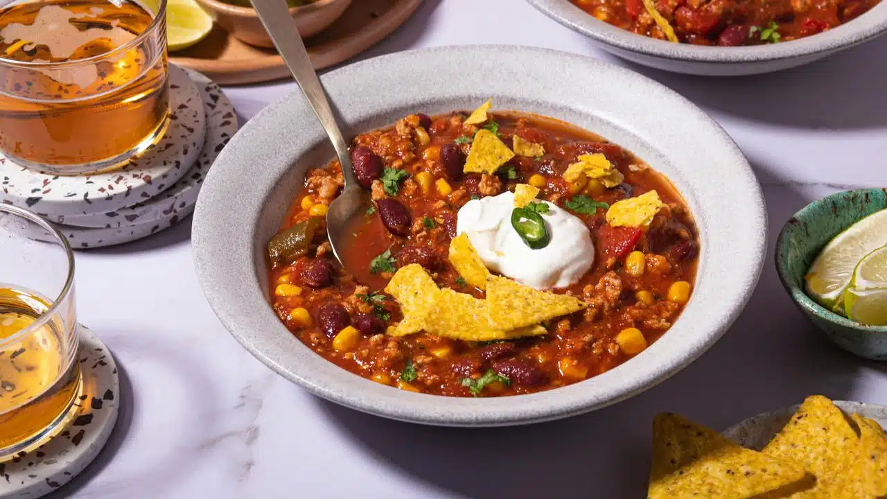 A bowl of chili with beans, corn, sour cream, and tortilla chips.