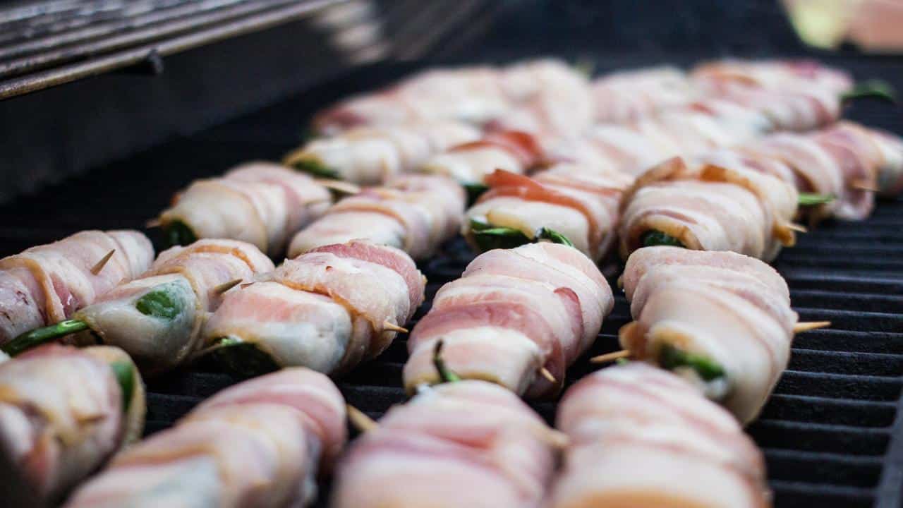 A grill with bacon-wrapped jalapeños cooking.