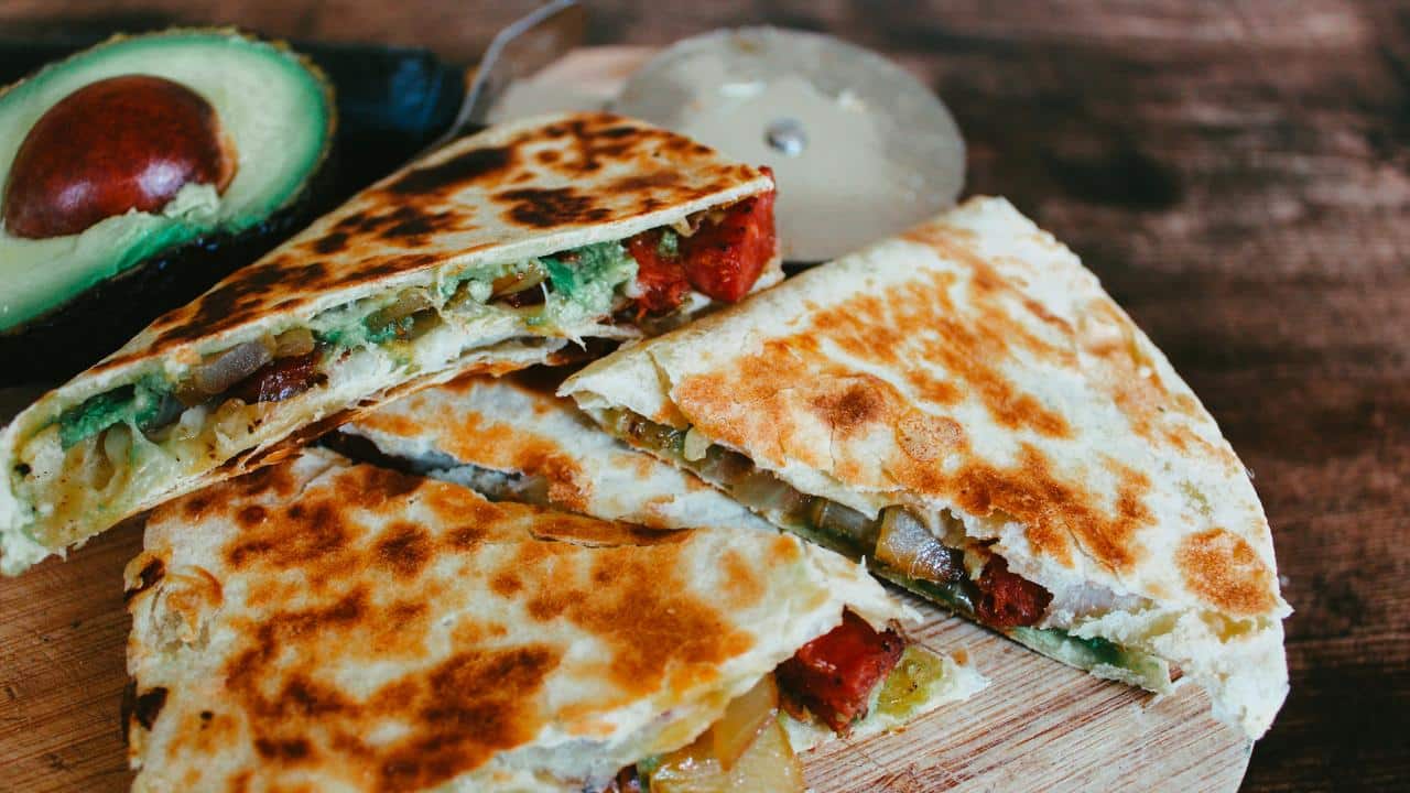 A sliced quesadilla with avocado on the side.