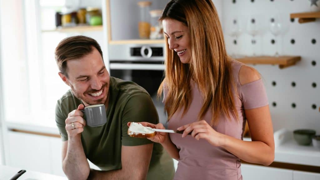 A couple smiles in the kitchen while preparing breakfast together.