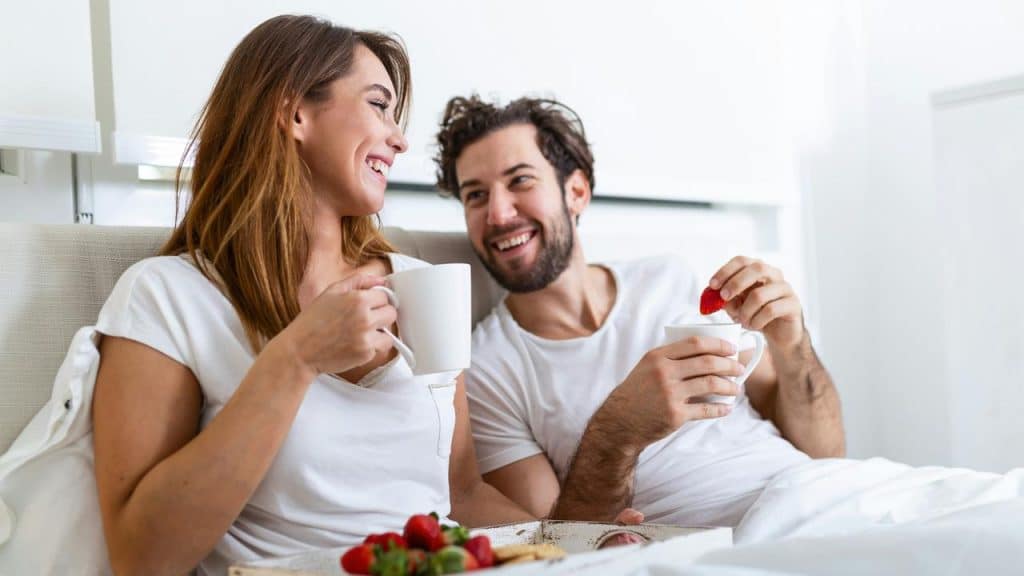 A couple enjoys breakfast in bed with coffee and strawberries.