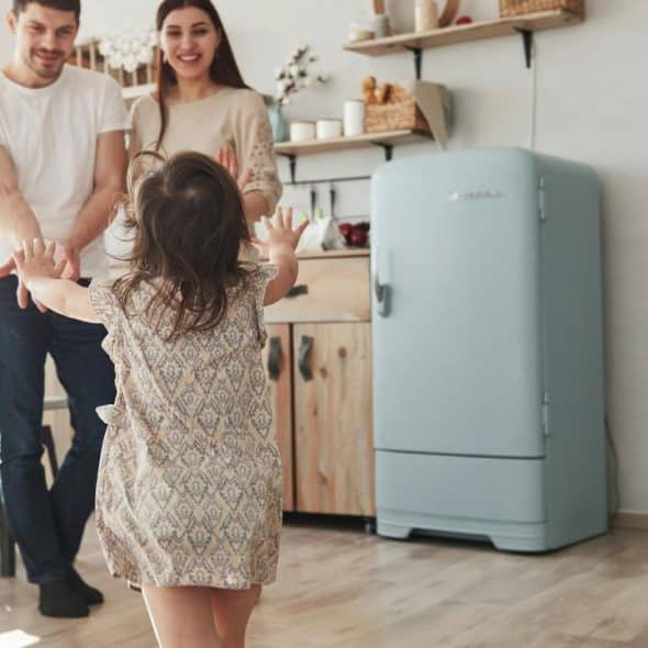 A young child runs toward smiling parents in a cozy kitchen.